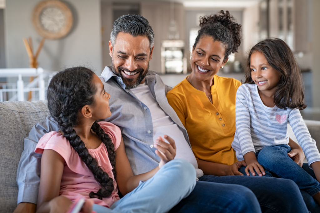 Family of four sitting on the couch and laughing together.