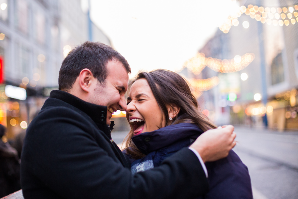 Couple on the street nuzzle noses and laugh together (a sign of relationship health).