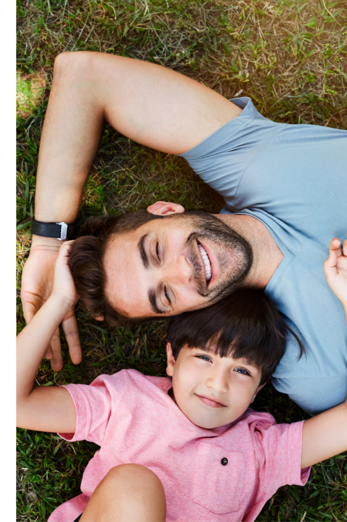 Dad and son laying on the grass looking up at the camera.